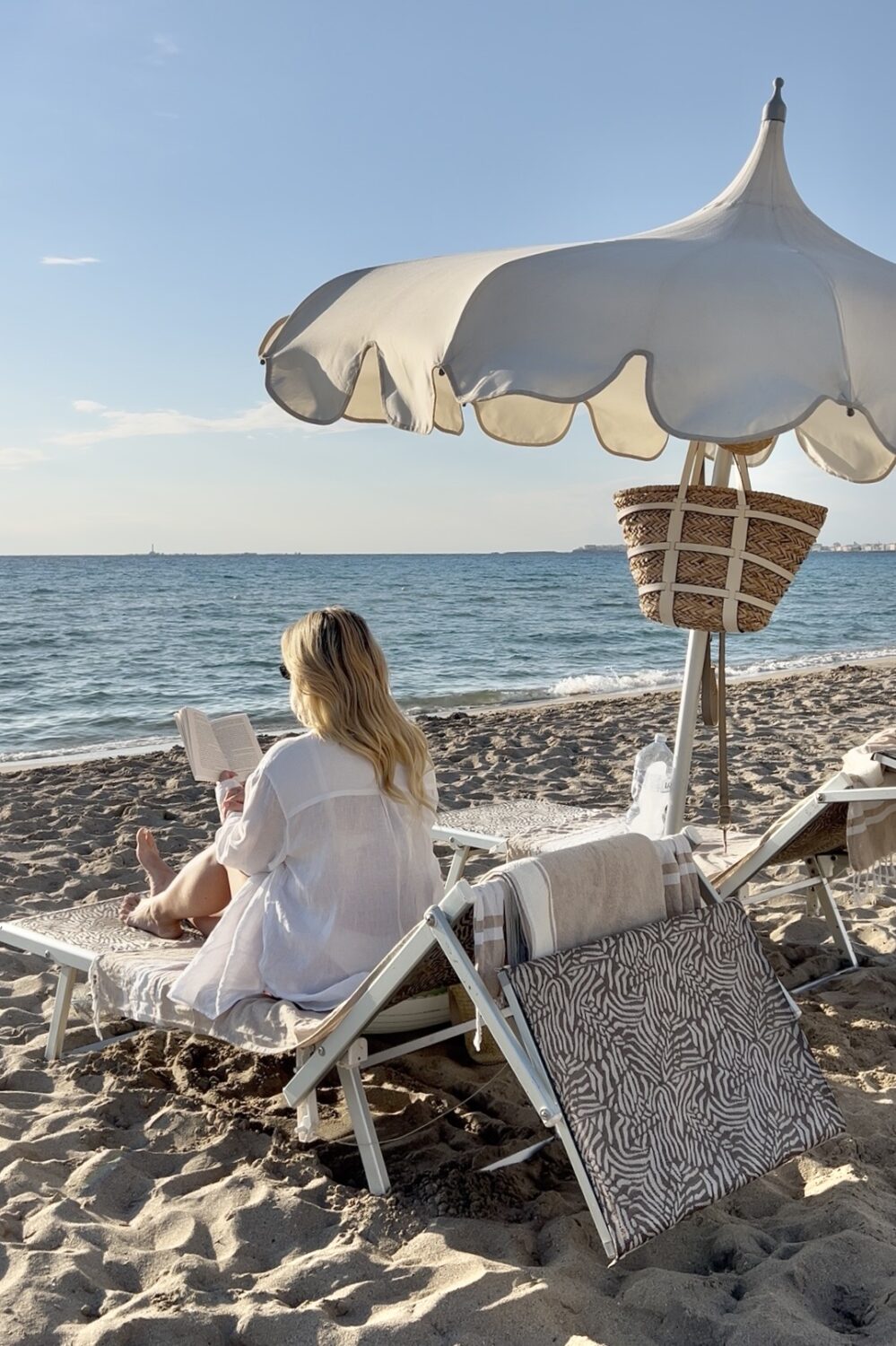 Entspannte Frau liest Buch am Strand unter Sonnenschirm bei Sonnenuntergang.
