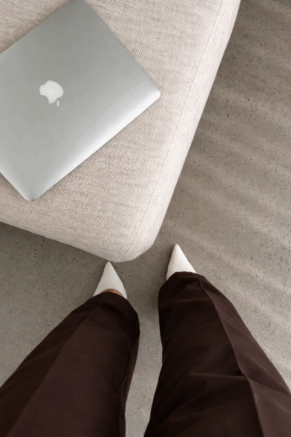 Eine Person steht vor einem Sofa mit einem Laptop auf dem Sitz, Blick nach unten.