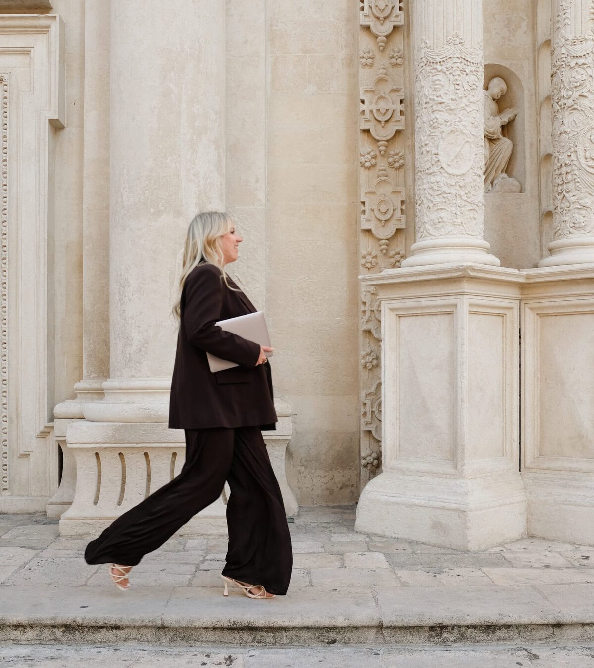 Eine selbstbewusste Frau in Businesskleidung beim Spaziergang vor einer historischen Architektur.