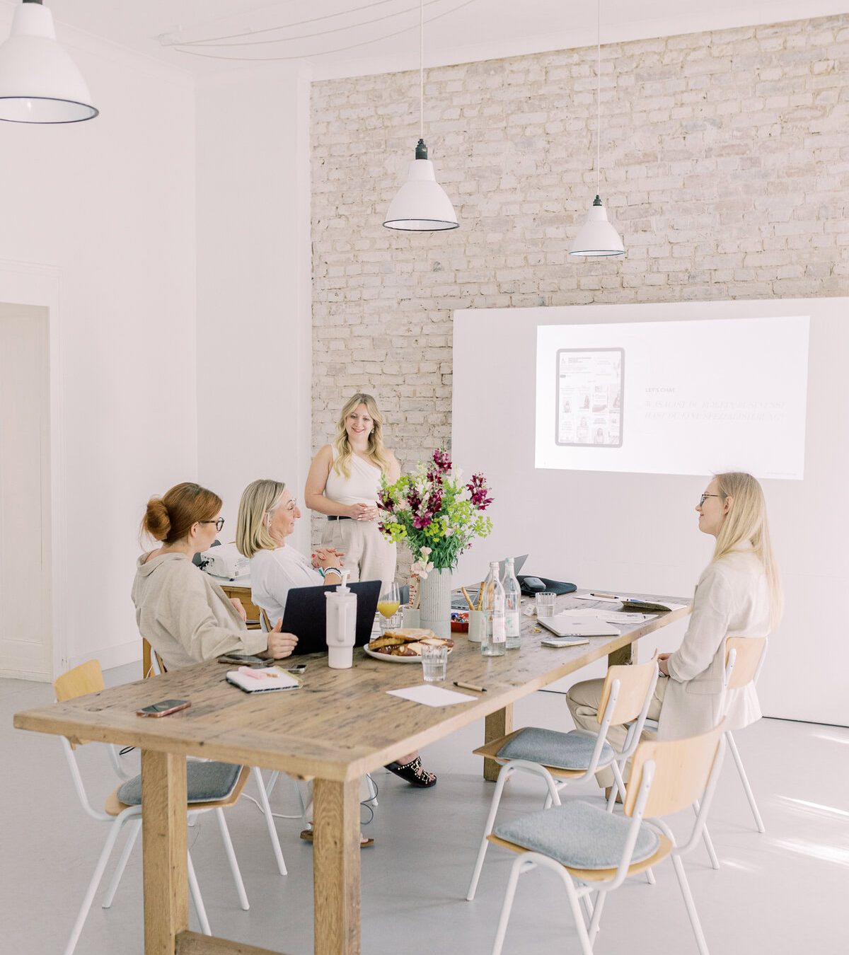 Frauen bei einer Besprechung im hellen, modernen Konferenzraum mit Whiteboard und Blumen.